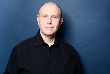 Christian Kahlert hat neben dem Beruf studiert. Portraitfoto Christian Kahlert vor blauem Hintergrund